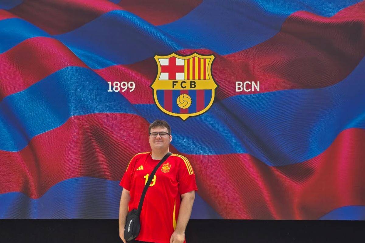 A man wearing a red and yellow sports jersey stands in front of a large FC Barcelona logo and a backdrop with red and blue stripes, perfect for fans exploring Barcelona in a day or hopping on the Barcelona city tour bus.
