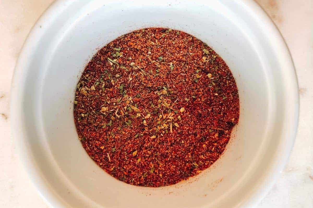 A white bowl filled with a reddish-brown spice mix, speckled with green dried herbs, sits on a light-colored surface—a perfect blend for an Easy Enchilada Recipe.