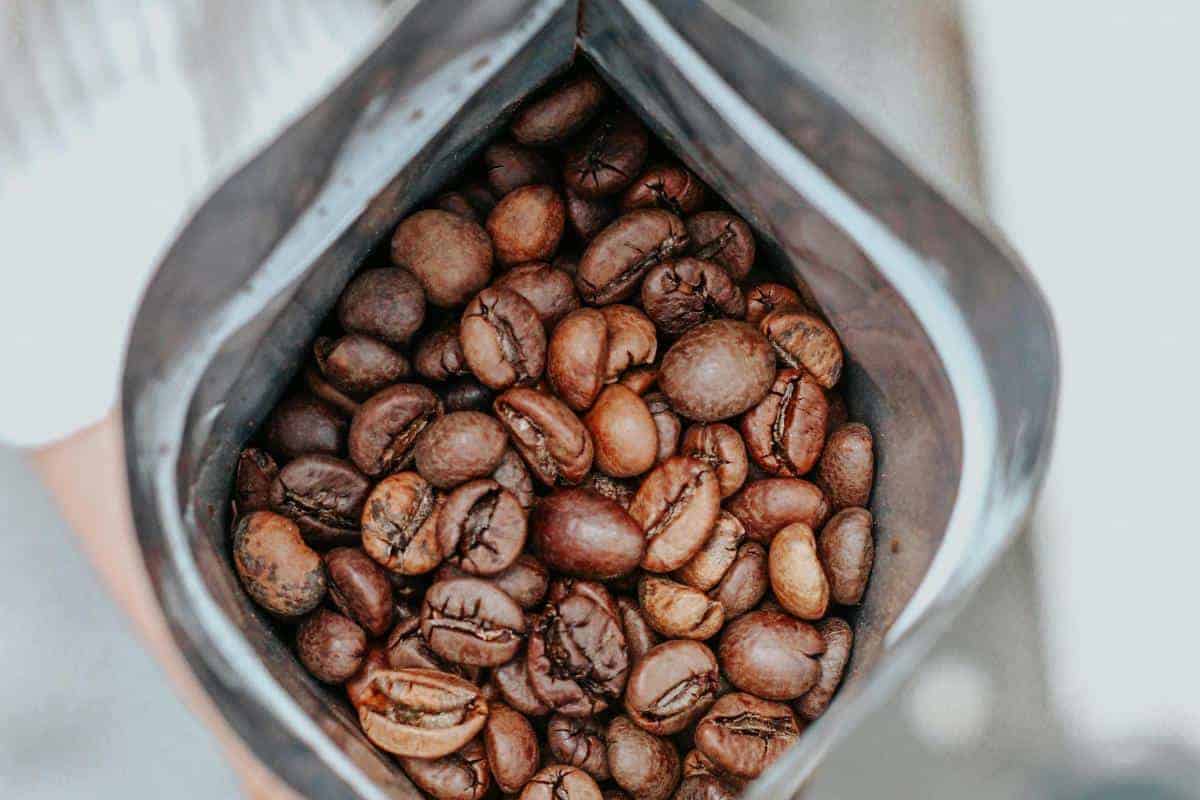 An open bag filled with whole roasted coffee beans, viewed from above, shows glossy brown beans inside a silver-lined package—perfect for those who enjoy the aroma of freshly ground beans.