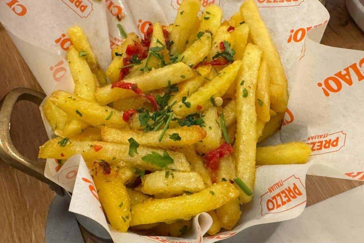 A serving of golden French fries topped with chopped parsley and red pepper pieces, presented in a paper-lined container with "PREZZO" branding—perfect for a quick bite at Prezzo Italian Nottingham.