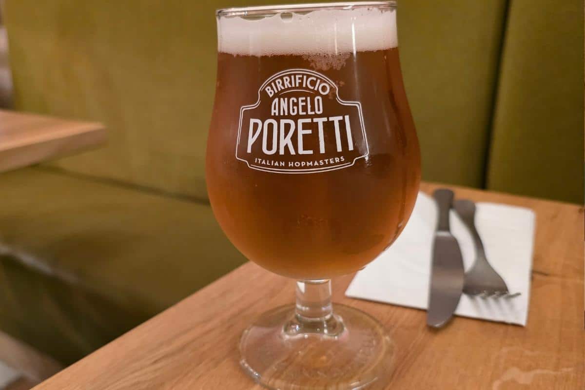 A tulip glass of amber beer with a foamy head, labeled "Birrificio Angelo Poretti," sits on a wooden table beside cutlery and a folded napkin—capturing the inviting ambiance of Italian cuisine at Prezzo Italian Nottingham.
