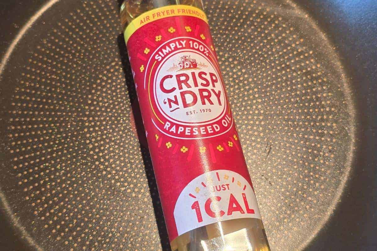 A bottle of Crisp 'n Dry rapeseed oil with a red label sits on a non-stick frying pan. The label highlights "just 1 CAL" and "air fryer friendly"—perfect for your Healthy Fakeaway or Ultimate Sticky Beef recipes.