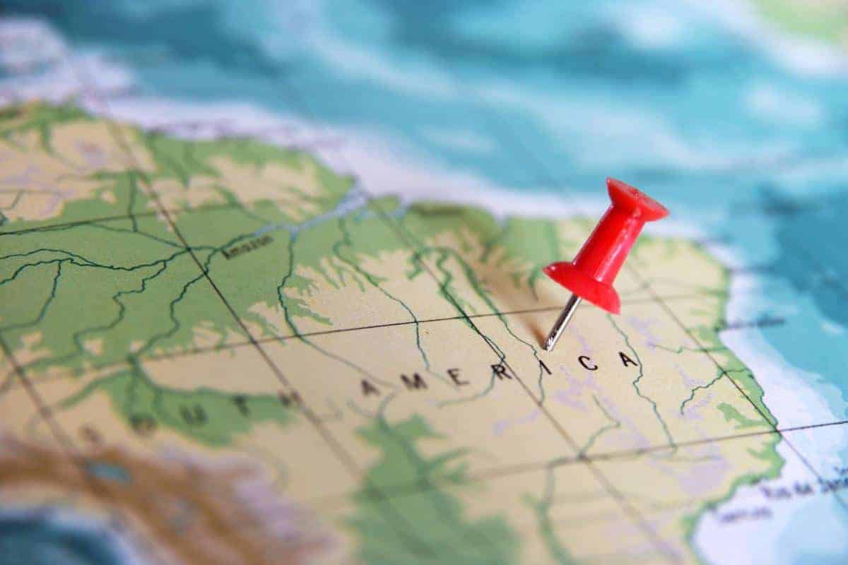 A red pushpin is placed on a map of South America, marking a location near the center of the continent—perfect for planning a South American trip. The map shows country borders, rivers, and topographical details in green and blue tones.