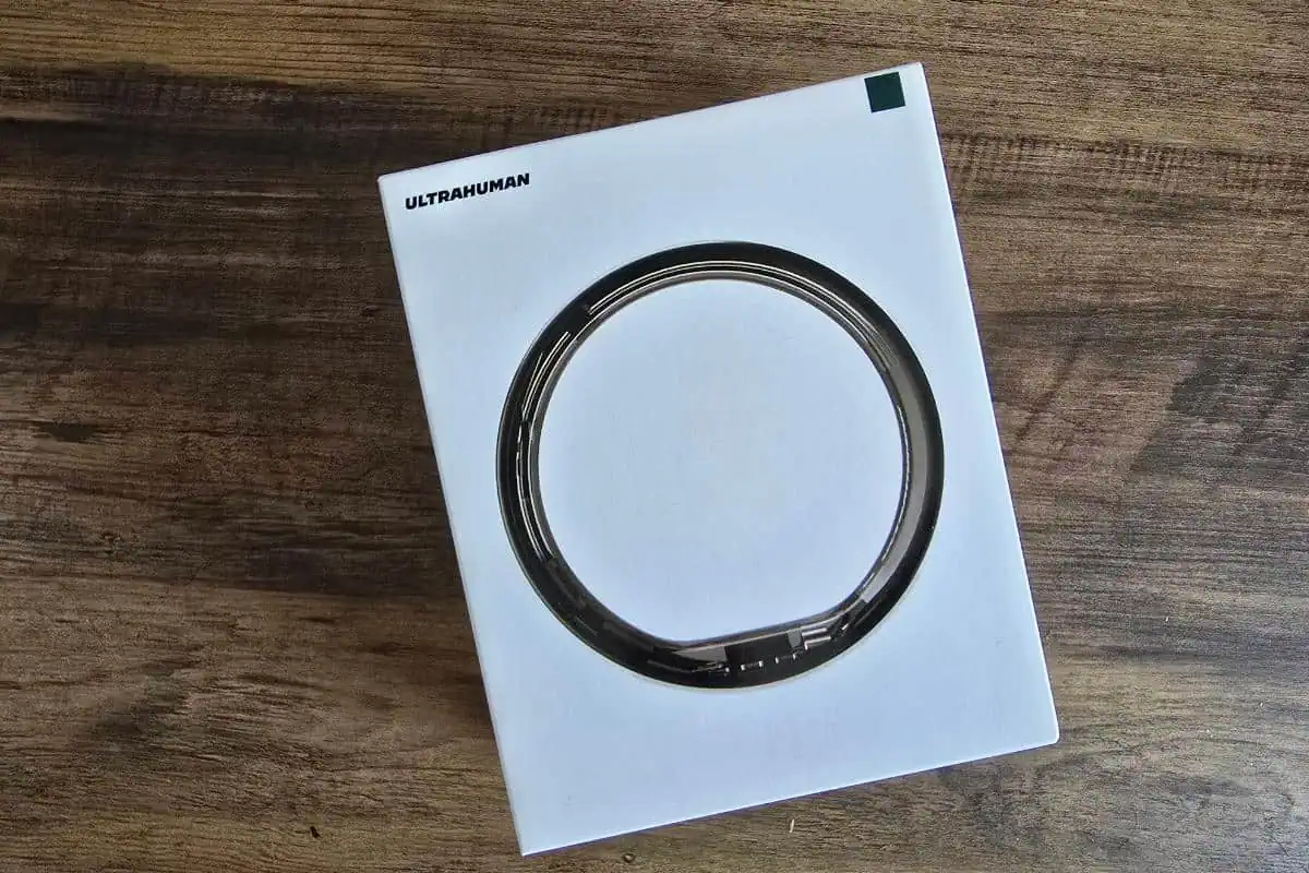 A white box with "ULTRAHUMAN" on the top left, featuring a large circular design in the center, sits on a wooden surface—perfect for anyone seeking an in-depth review of the Ultrahuman Ring Air smart ring.