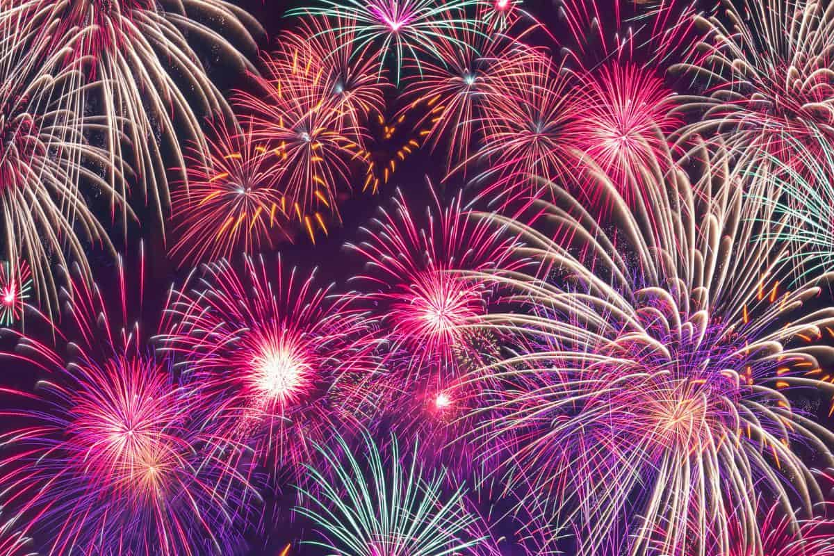 Colorful fireworks burst across a dark Bonfire Night sky, filling the scene with vibrant red, pink, orange, and white streaks, celebrating a festive occasion with dazzling light and energy.