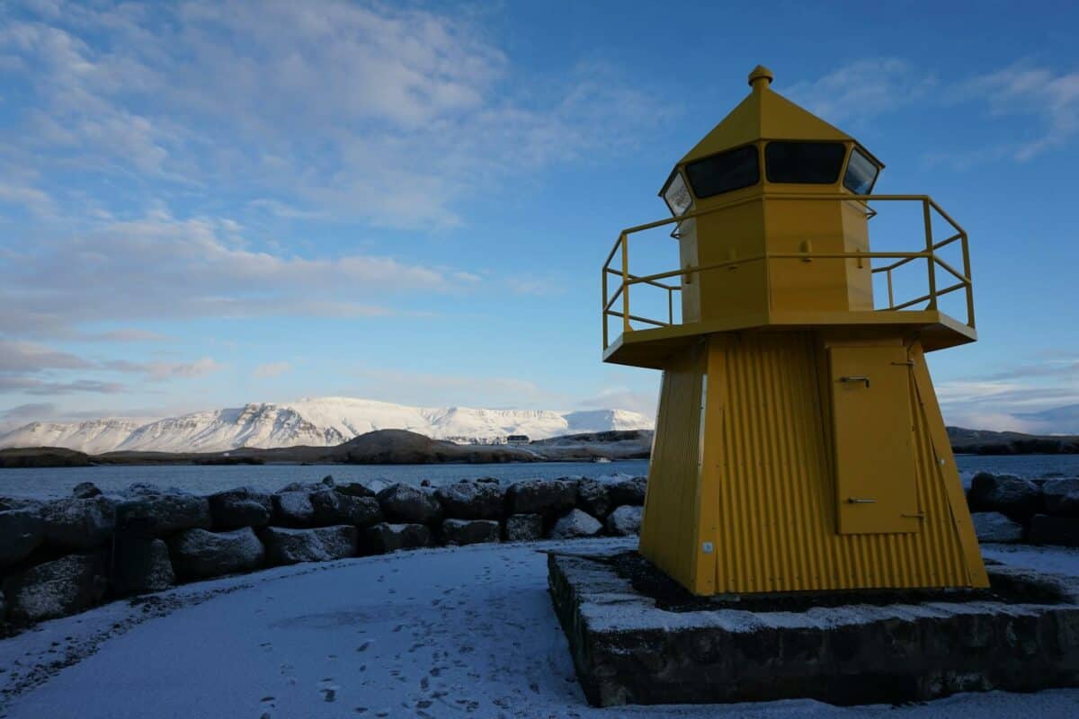 yellow and gray lighthouse in front of mountains