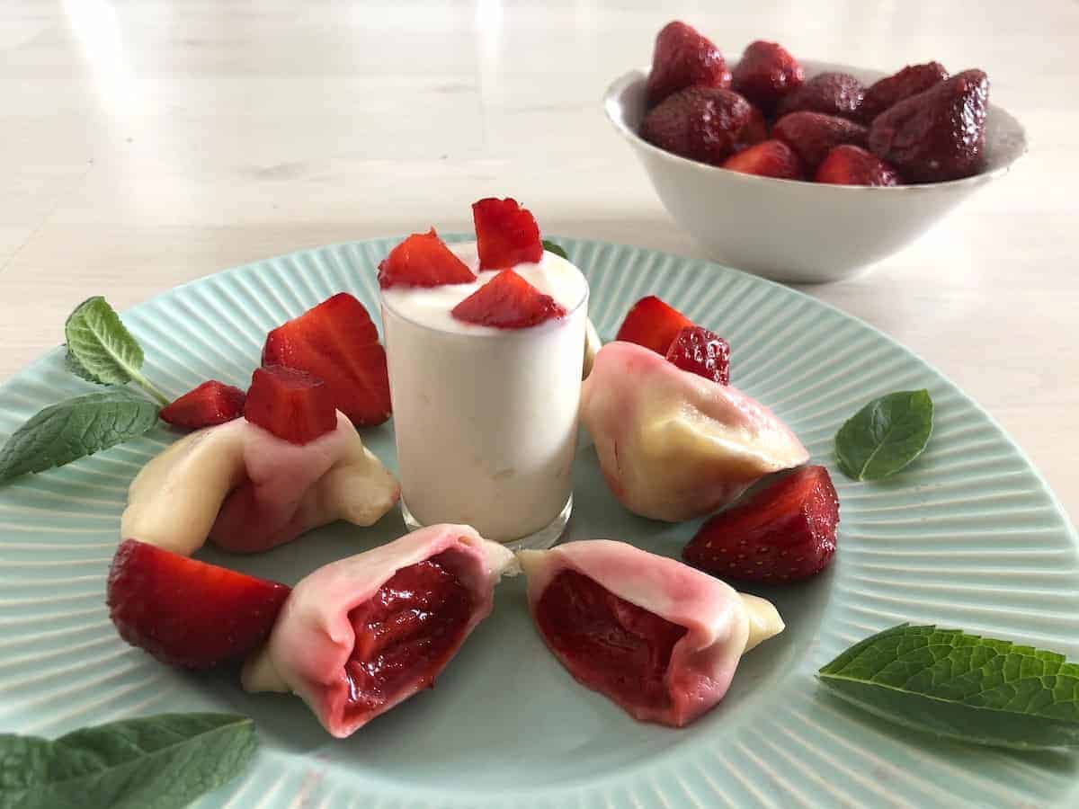 A plate with strawberry dumplings and cream on it.