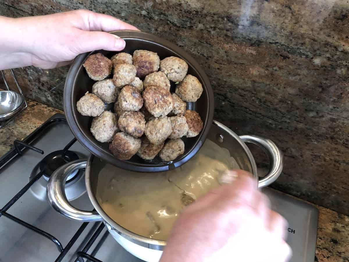 Klopsiki meatballs being added to a pot.