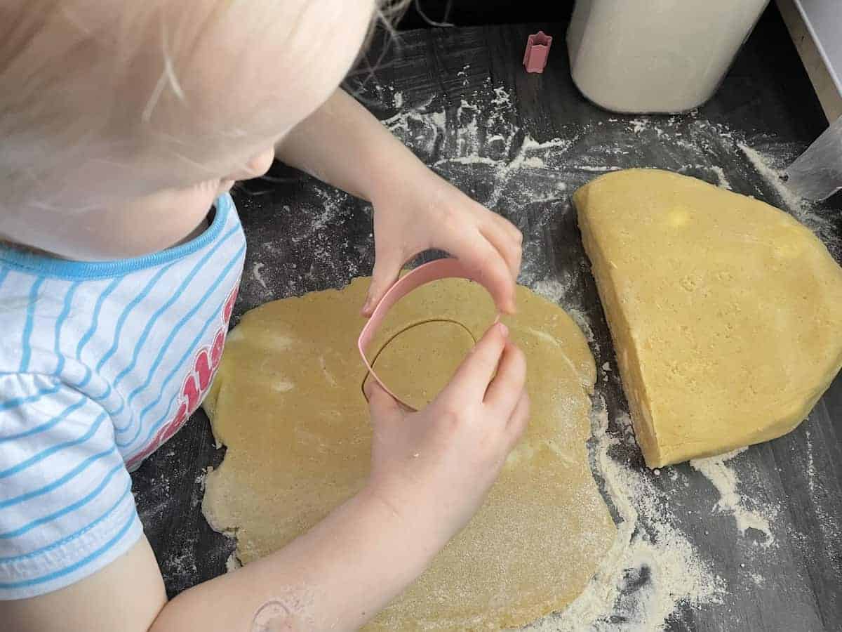 Child using cookie cutter on dough.