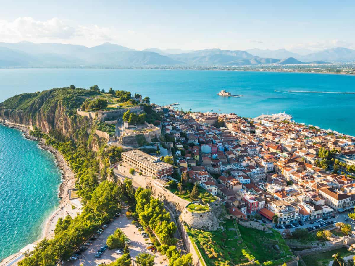 Travel Guide to Nafplio in Greece Travel Guide to Nafplio in Greece. Aerial view of Nafplio surrounded by blue sea and mountains in the background.