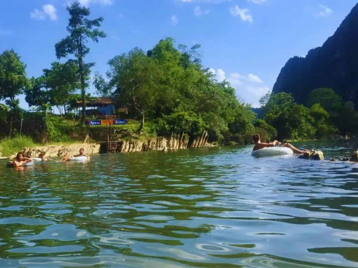 Vang Vieng Tubing in Laos Vang Vieng tubing - tourists floating in white rubber rings on the river in Vang Vieng in Laos. The river bank is lined with grass and green trees with mountains in the background to the right.