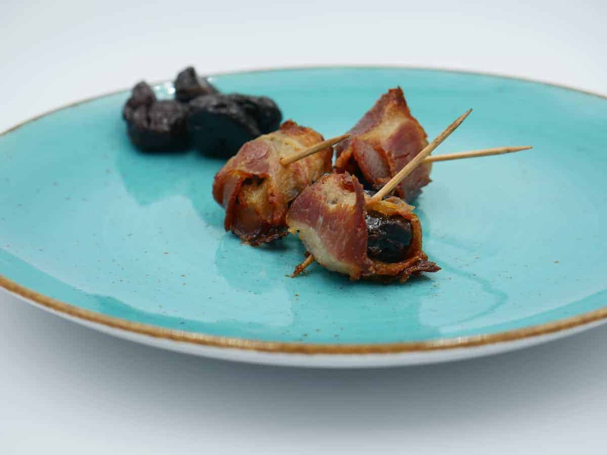 Prunes wrapped in bacon on a blue plate.