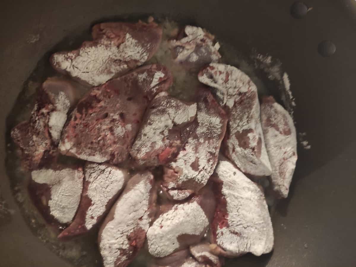 Uncooked pork liver covered with flour frying in oil.