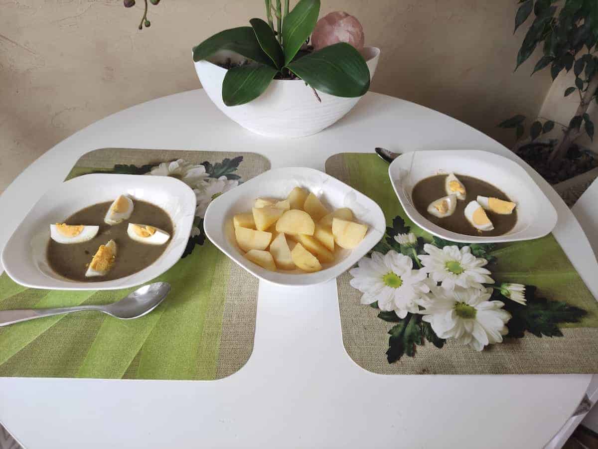 Bowls of sorrel soup with boiled eggs on top and boiled potatoes in another bowl.