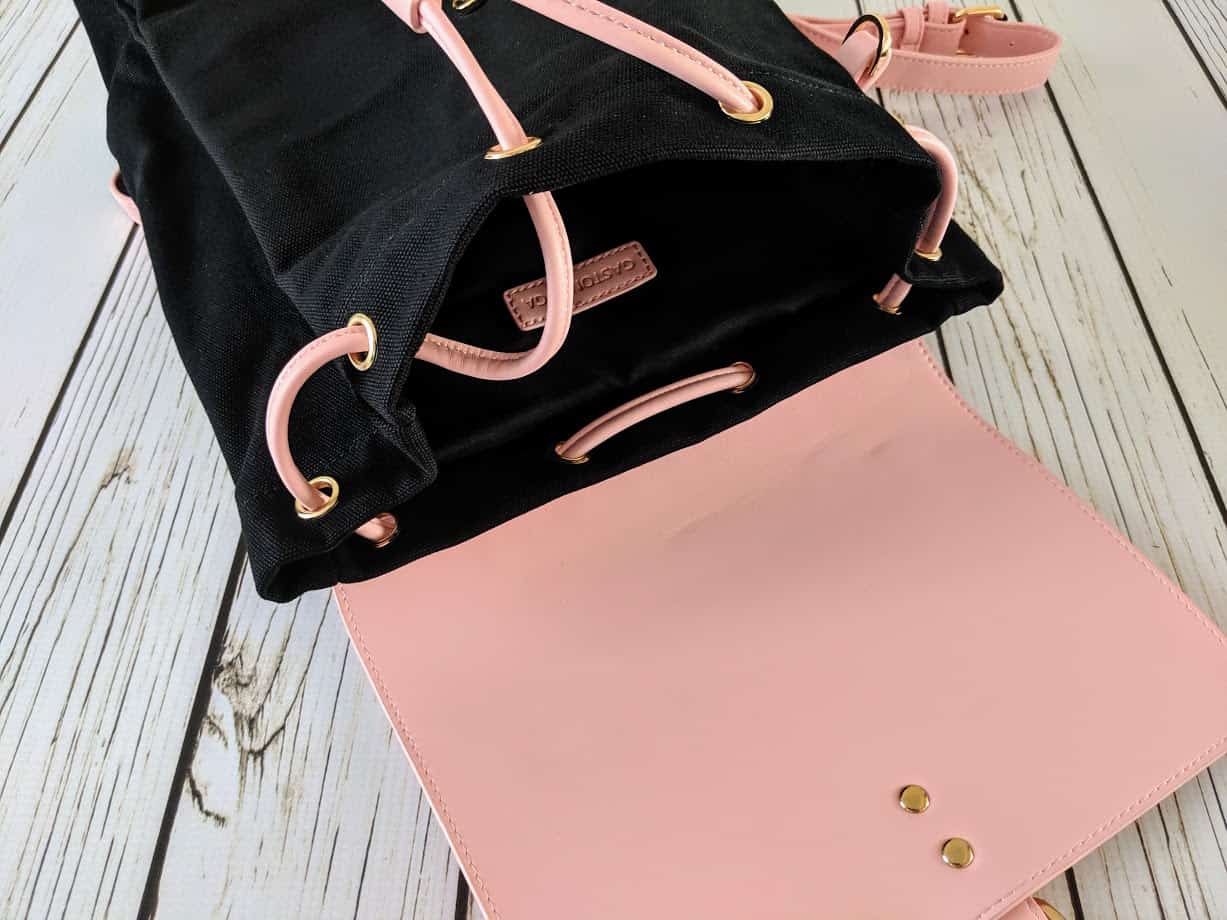 An open pink and black backpack on wooden surface