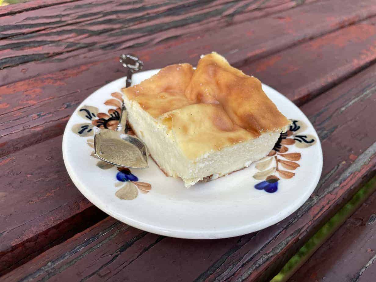 A gluten-free Polish cheesecake recipe - Sernik Bezglutenowy, served on a plate on a wooden bench.