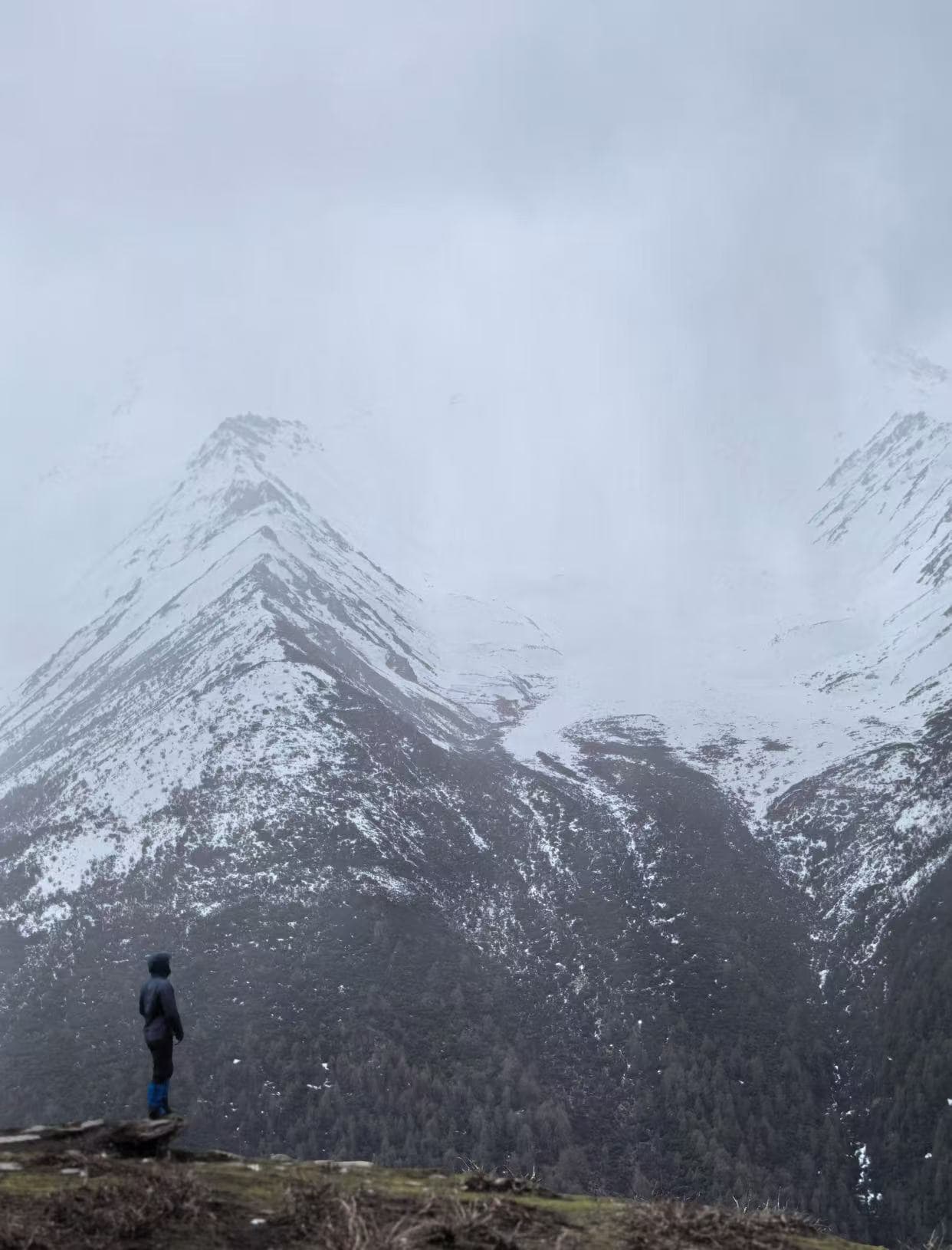 Trekking professional conducting terrain visualization and high-altitude adaptation on a mountain ridge under challenging weather conditions. Expedition planning and field verification.