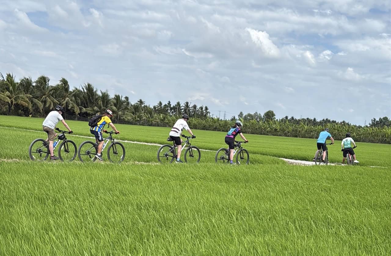 Cyclists exploring the Mekong Delta in Vietnam on an Indochina backroads cycling expedition, riding through riverside villages, lush farmland, and scenic canal-lined roads.