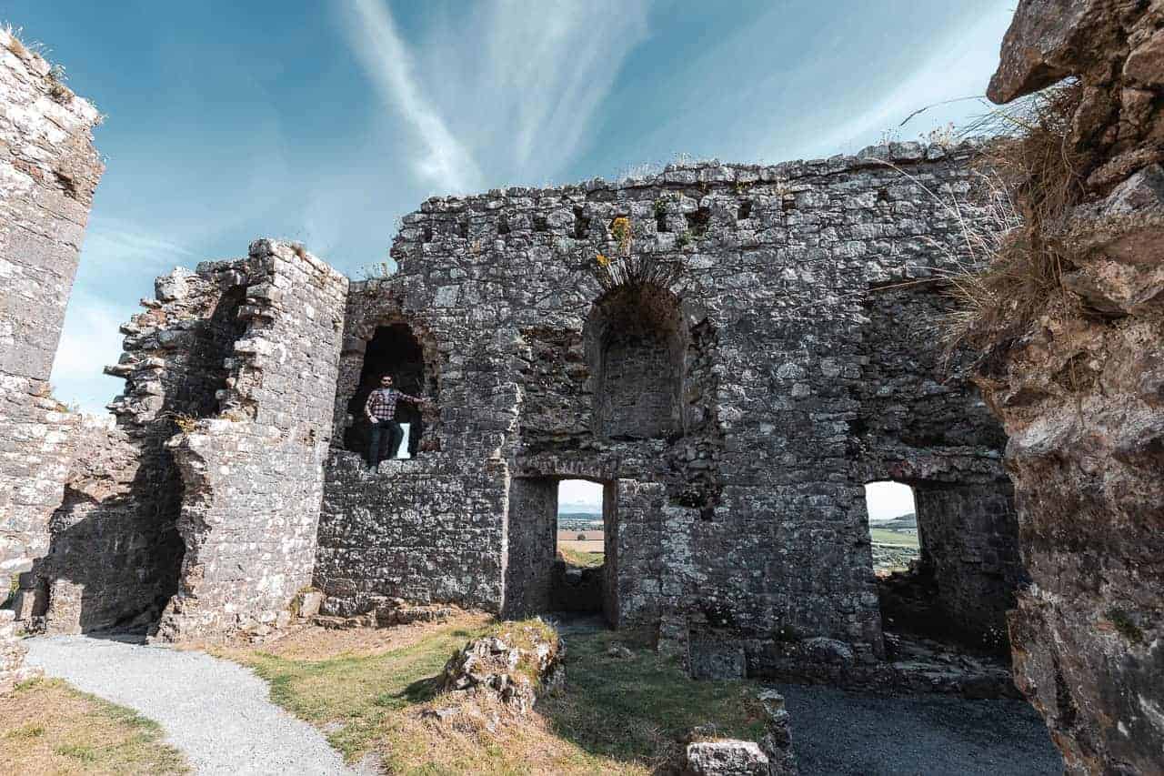 The interior of the Rock of Dunamase ruins, showing a man standing in one of the arched windows of the crumbling stone walls.
