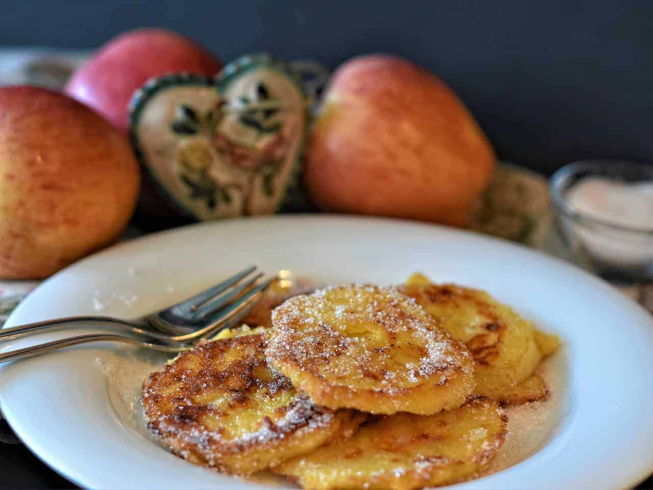 Plate of racuchy pancakes next to apples.