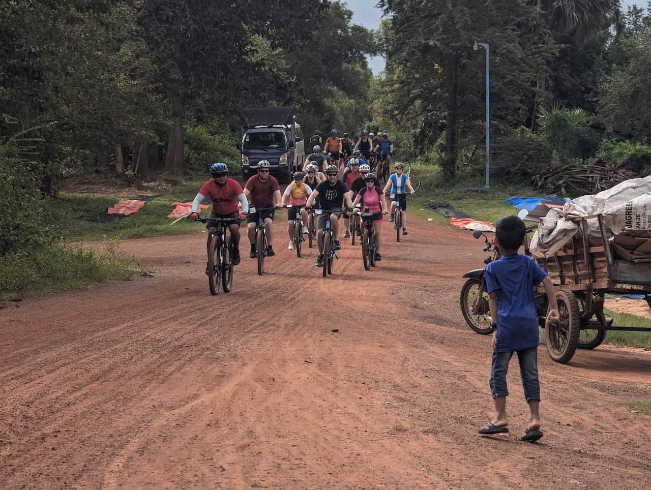Cyclists riding through rural Cambodia villages, passing traditional Khmer homes, rice paddies, local farms, and peaceful countryside roads on a journey to Siem Reap and Angkor Wat.