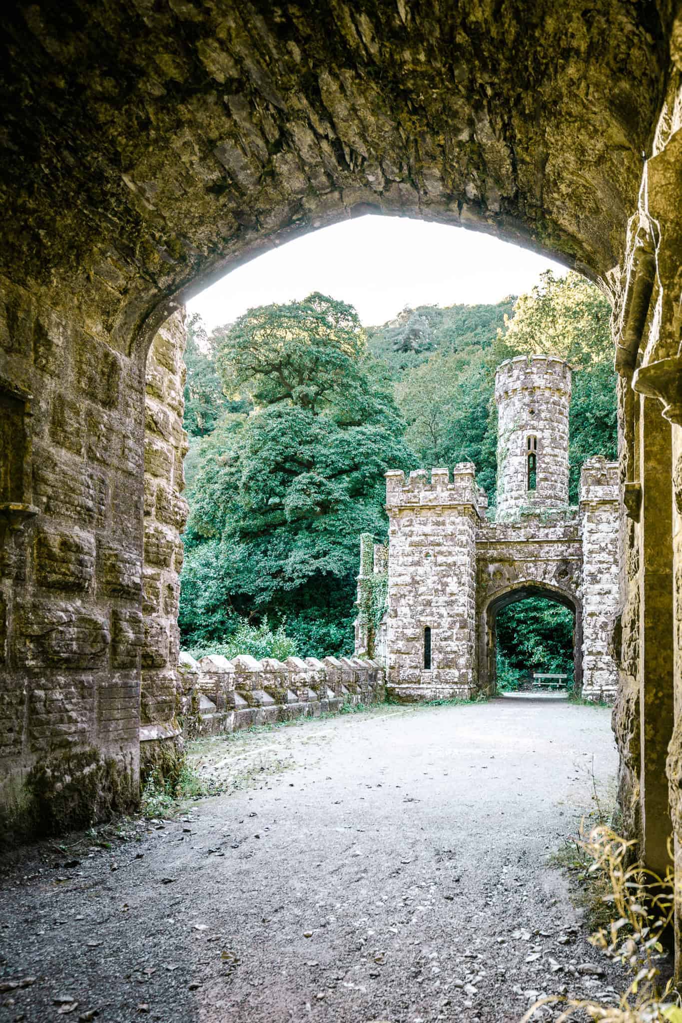 A dramatic angle of Ballysaggartmore Towers viewed from the bridge, with the castle partially hidden by overgrown vines and surrounded by a dense forest.