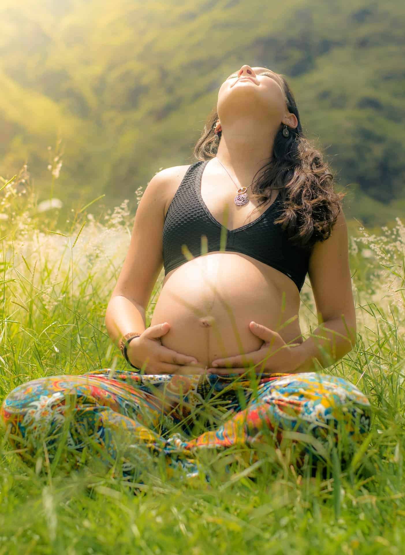 Brunette woman sitting in grass with both hands on baby bump