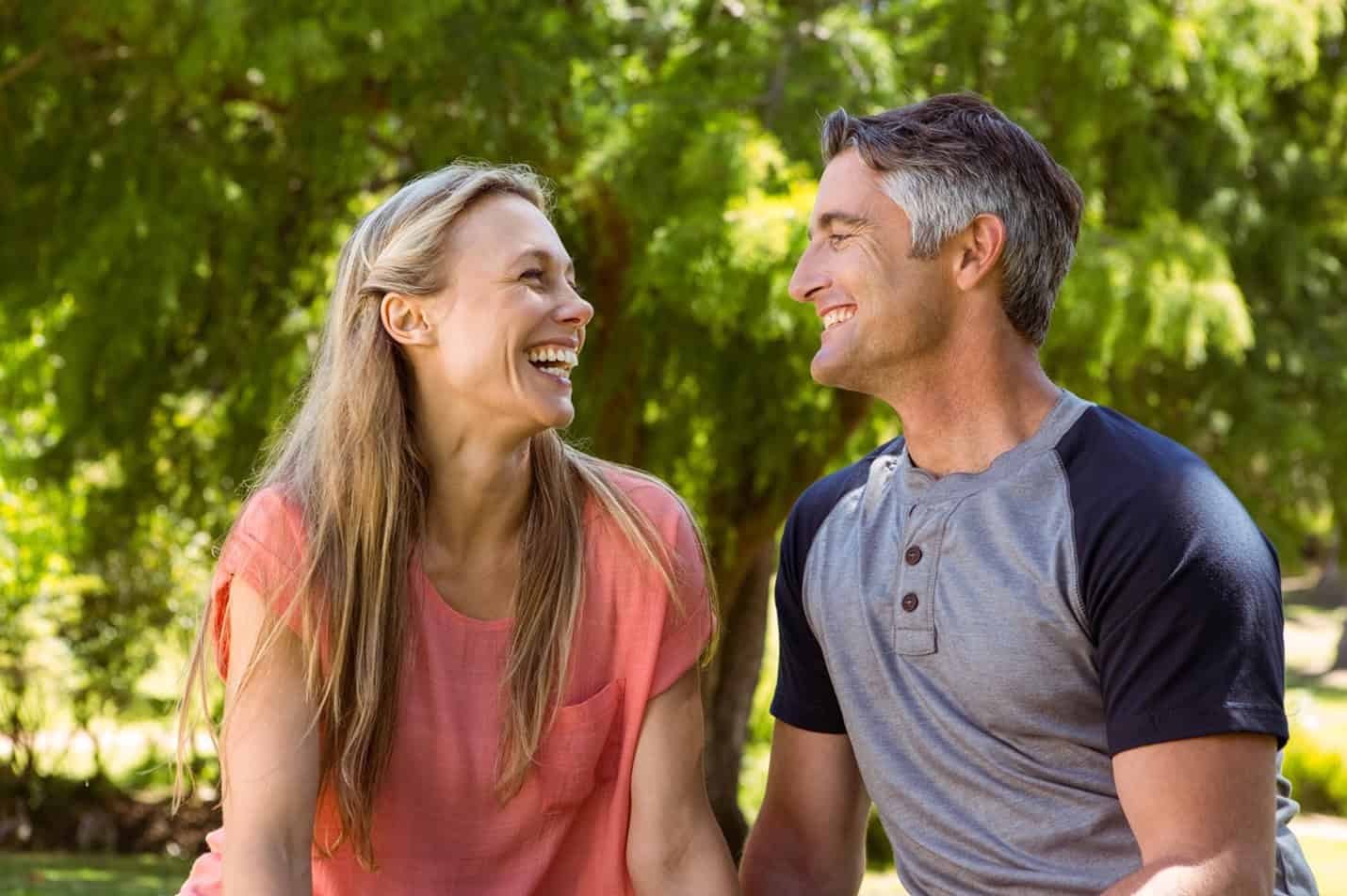 Joyful couple sitting outside and smiling at each other, no longer wondering what the signs are to knowing you've found the one?