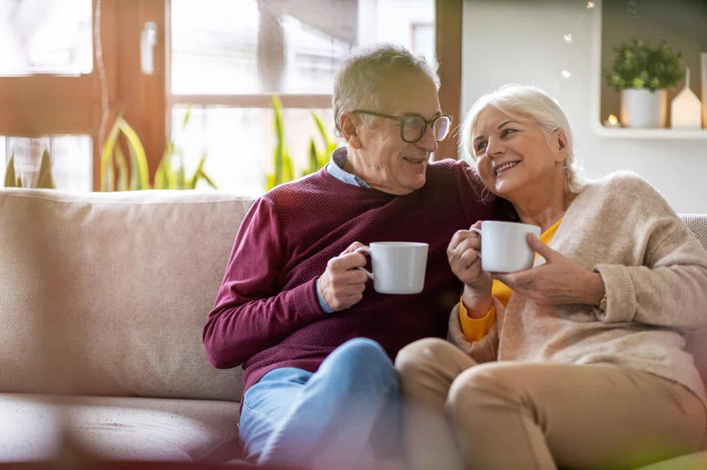 Happy mature couple cuddling on the couch with coffee because they improved their chances of finding love after 60.