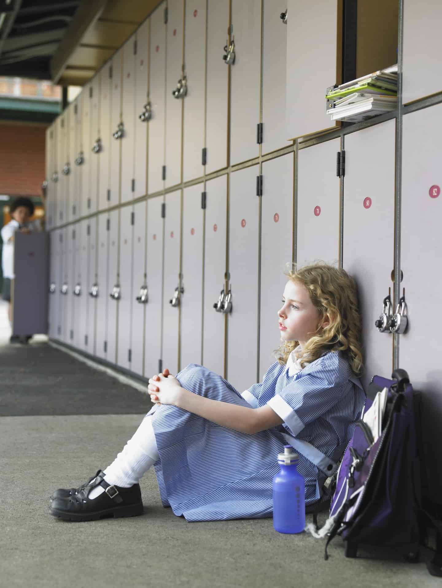 girl sitting in front of lockers looking unhappy