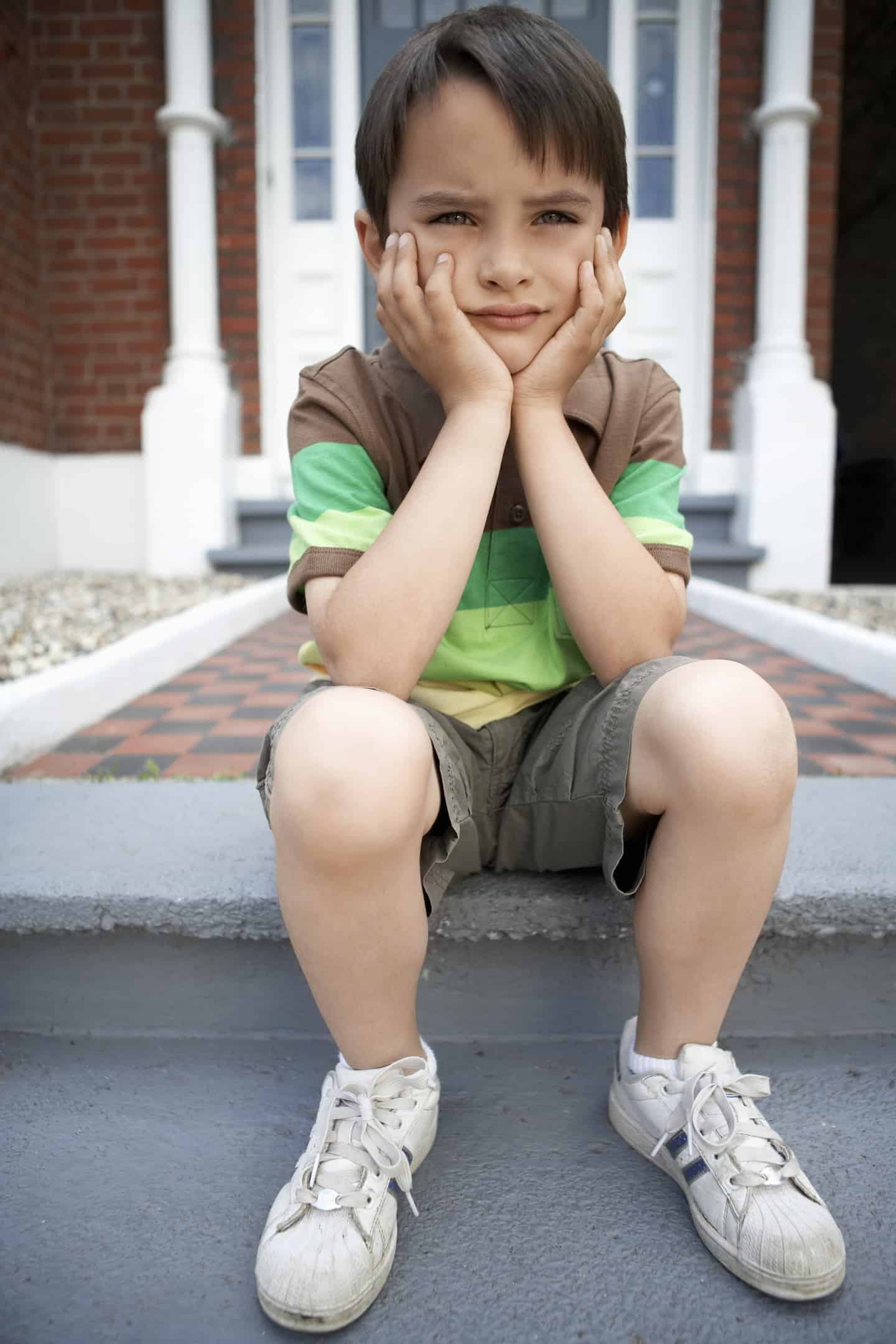young boy sitting on a step hands at his chin looking sad