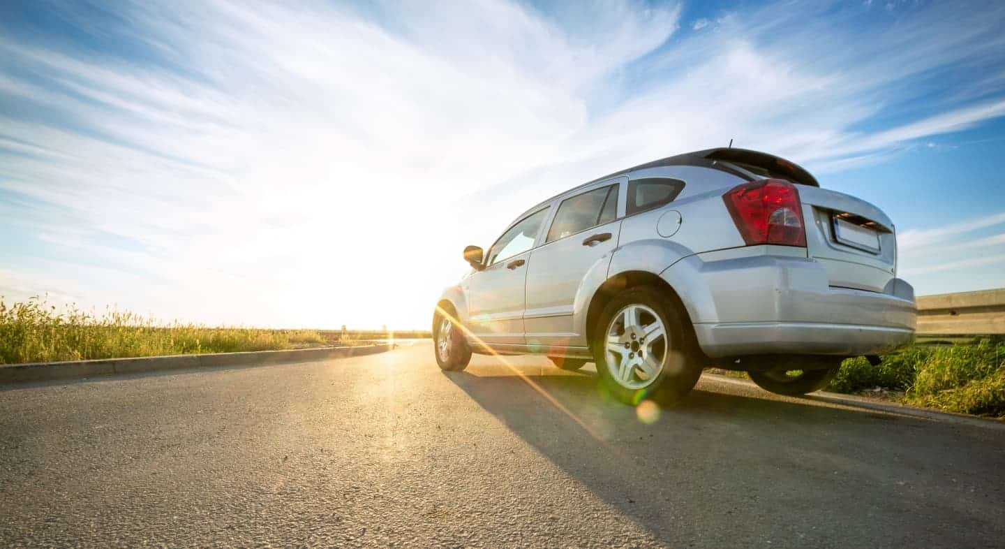 A silver car parked on the side of a road with the sun shining on it