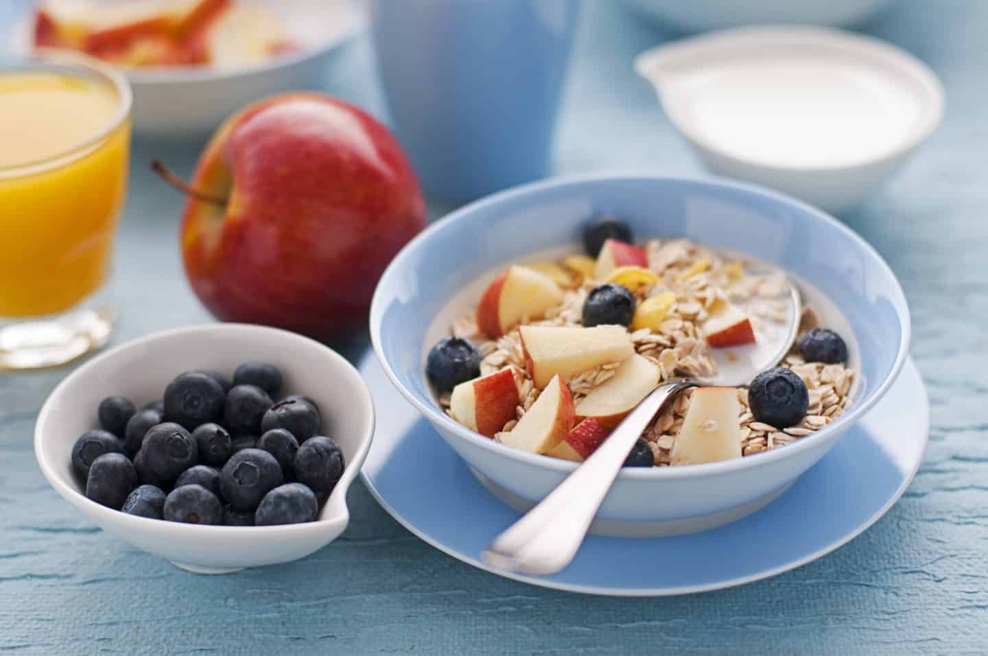 healthy breakfast of apple, blueberries and a bowl of muesli with both in on a table