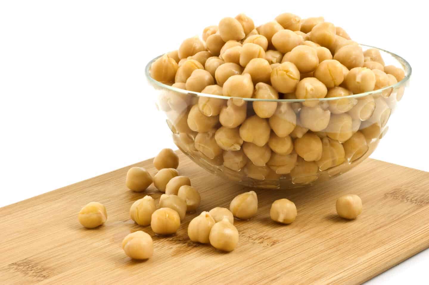 Washed and drained canned chickpeas in glass dish on bamboo board
