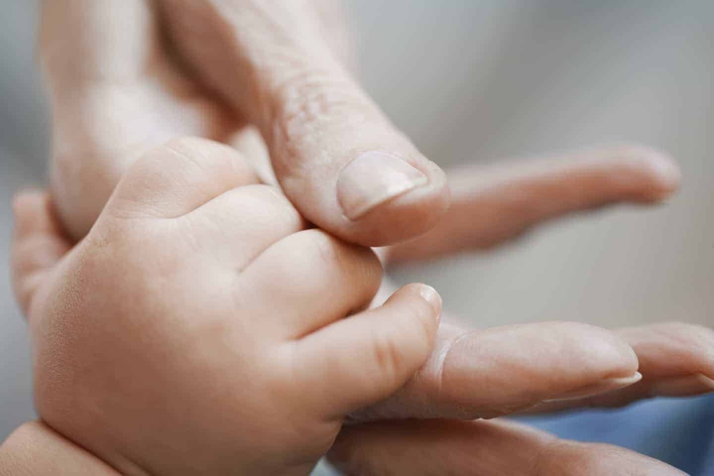 Closeup of an older person\'s hand holding babies hand
