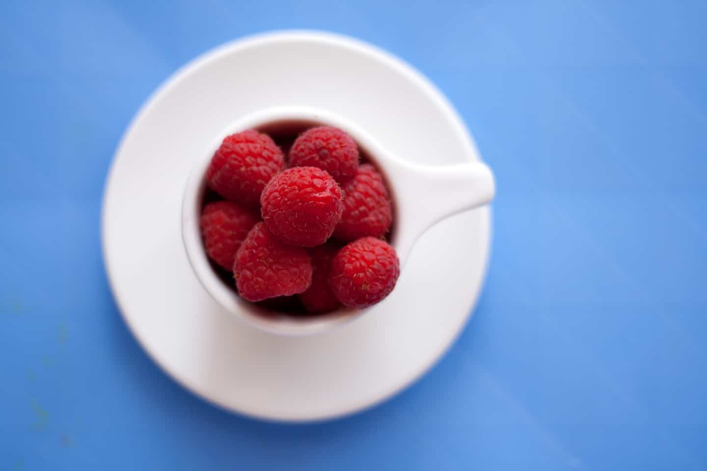 Pot of raspberries on blue surface