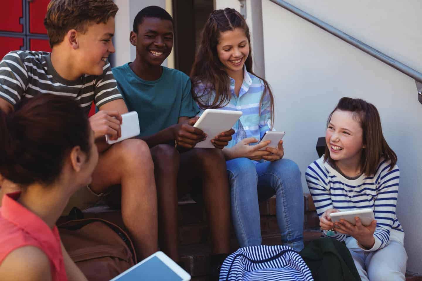 group of teenagers sitting on steps with phones and tablets