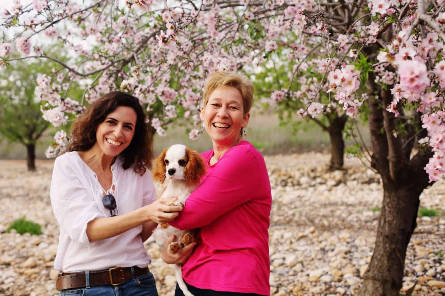 two ladies with a dog in a woods with pink blossom on the trees