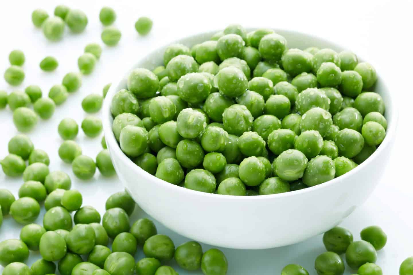 bowl of frozen peas with them spilt on the table