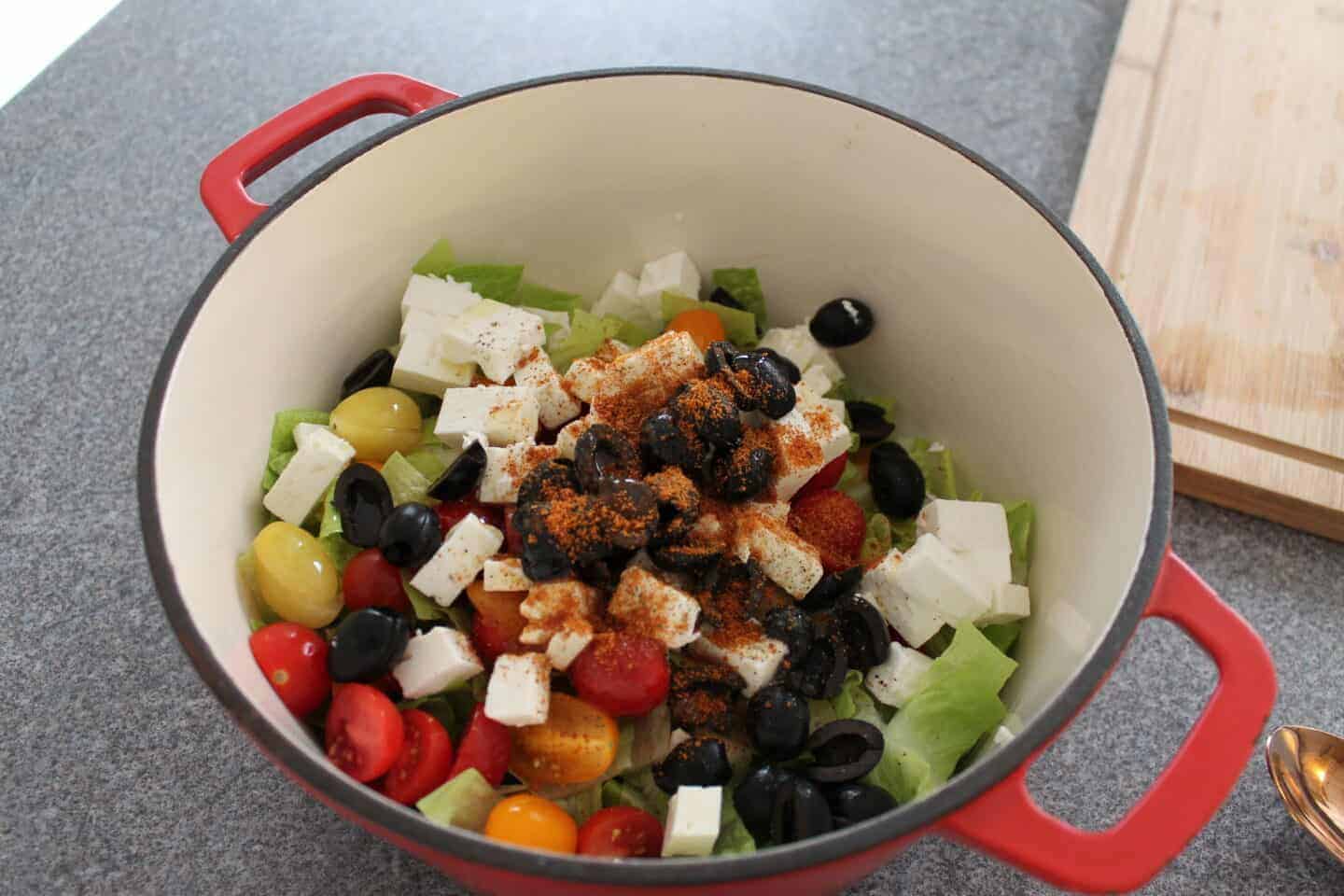 spices on top of the greek salad ingredients in the pan