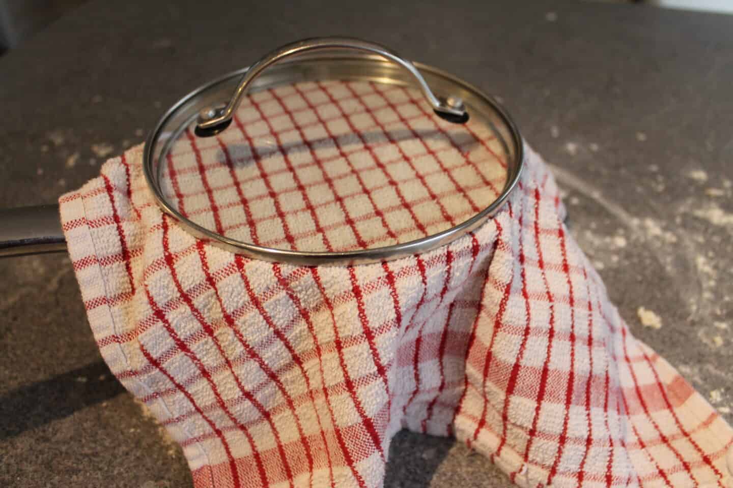 pizza dough in a pan with tea towel and lid to make a seal