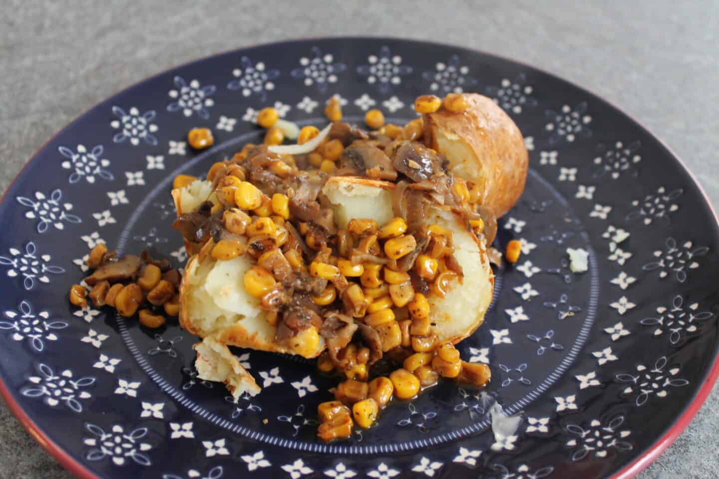 Jacket potato on a blue patterned plate topped with mushroom onion and sweetcorn topping