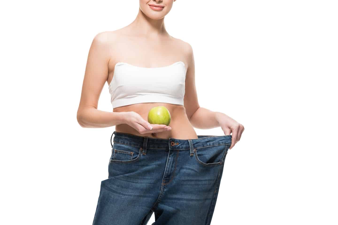 Lady holding large jeans away from her slim body with an apple in her hand on the Slimming world SP plan