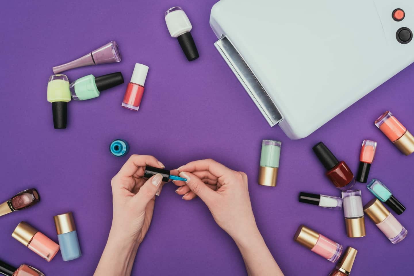 Hands with nail polishes surrounding them on purple background