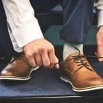 person tying brown leather shoes