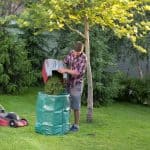 Gardener empty mower basket full of cuttings into plastic sack in garden