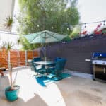 Outdoor patio at 3164 Thorn Street in North Park featuring a concrete seating area with a dining table and umbrella, a Weber gas grill, and a dark wood privacy fence accented by overhead string lights.