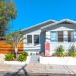Exterior front view of the Craftsman bungalow at 3164 Thorn Street in North Park featuring light blue lap siding, decorative red brick pillars, and low-maintenance desert landscaping with a horizontal wood gate and driveway.