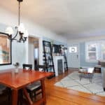 Modern open-concept living and dining space at 3764 Alabama in North Park with warm hardwood floors, a vintage-style chandelier, and a bright living area featuring a fireplace and large windows.