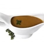 A slimming world friendly gravy boat filled with brown onion sauce, garnished with a small sprig of herbs, isolated on a white background.